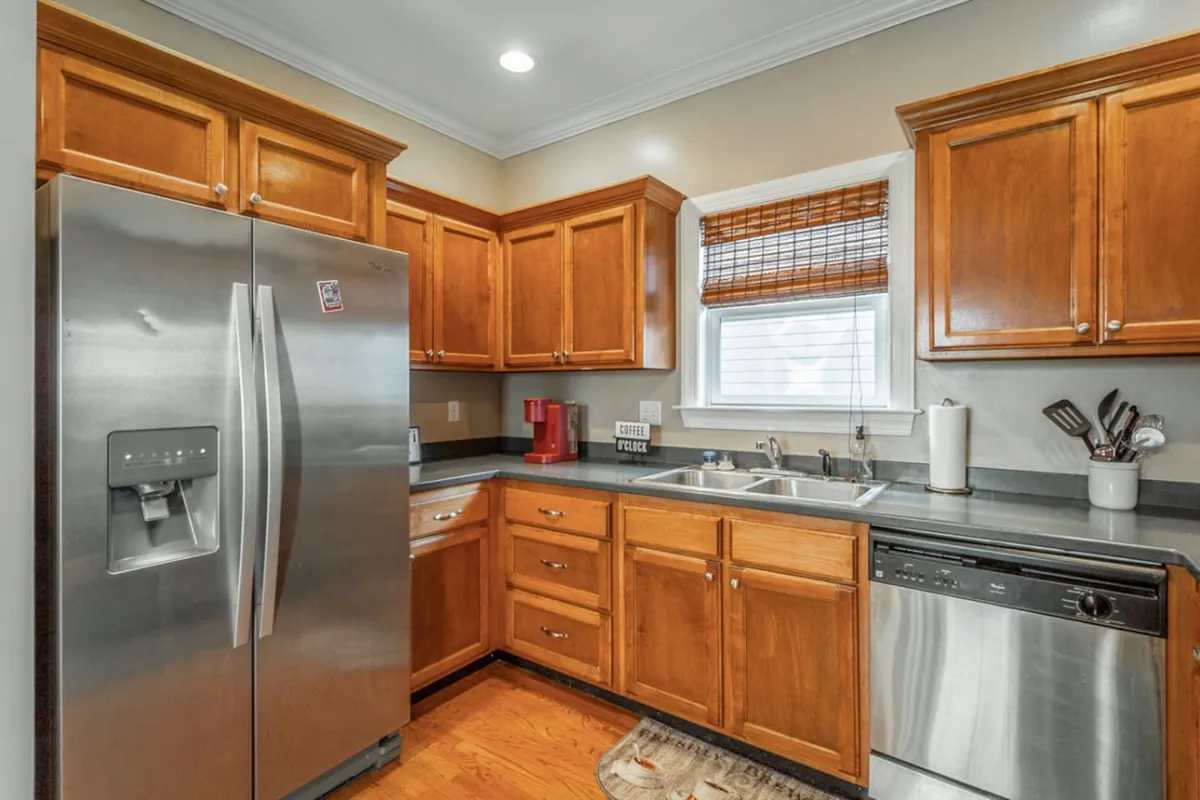 A bright, welcoming kitchen with stainless steel appliances, wooden cabinets, and a large window with blinds that lets in natural light. The space is organized and inviting, suggesting a comfortable spot to start the day or unwind after work.