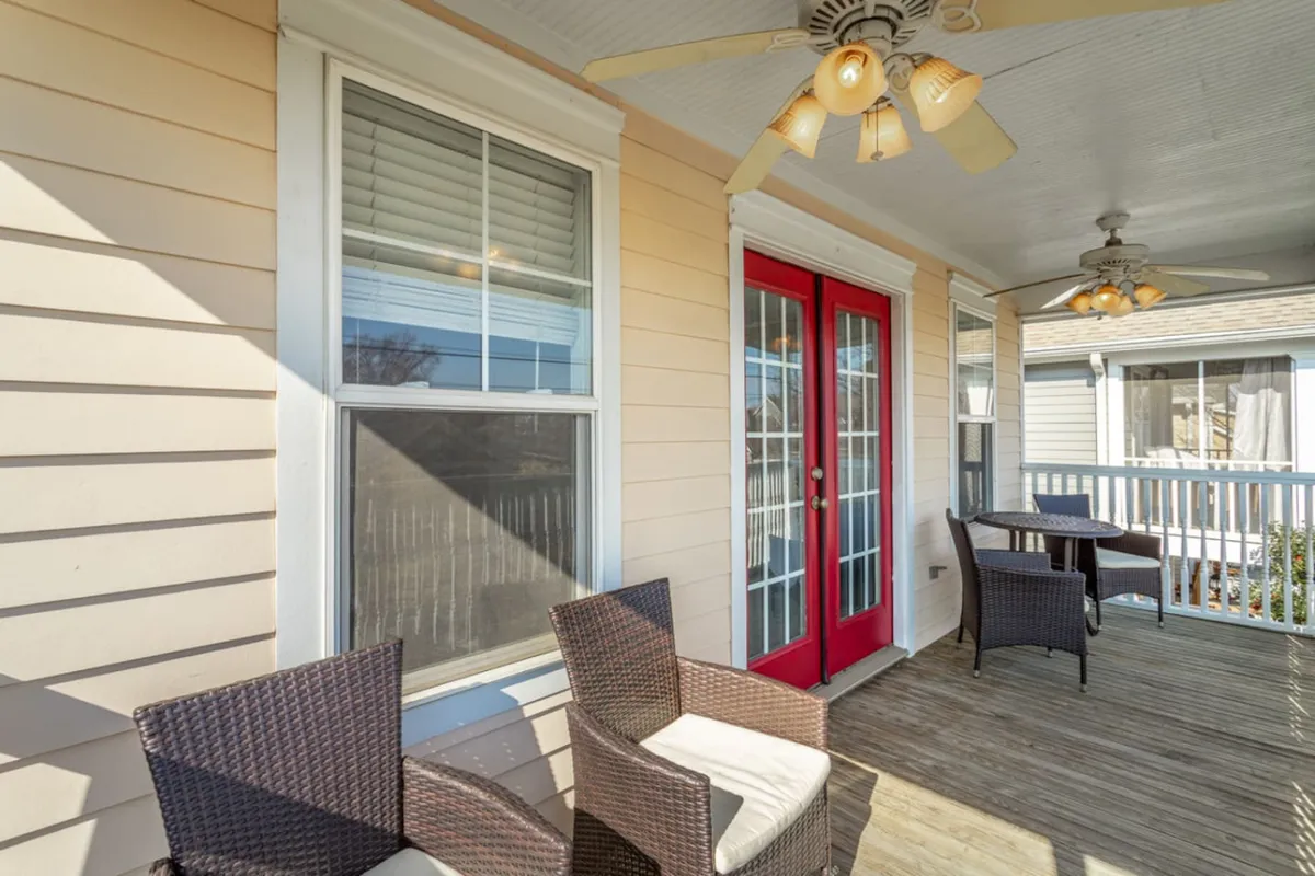 The image shows an exterior view of red double doors with comfortable wicker chairs and ceiling fans on the porch. It exudes an atmosphere of hospitality and quiet relaxation, hinting at private moments together before or after venturing out.