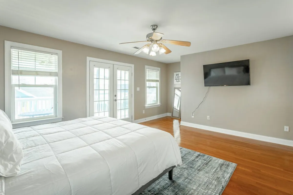 A serene bedroom with a comfortable bed, large windows bringing in natural light, ceiling fan, and a TV. The space looks peaceful, ideal for a restful night's sleep or a quiet evening after a busy day downtown.