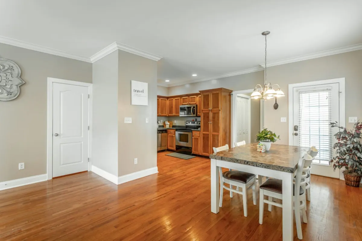 A dining area featuring a stylish table and chairs, adjacent to a kitchen and decorated with wall art. The space looks ideal for casual meals or informal gatherings, reflecting a warm, communal atmosphere.