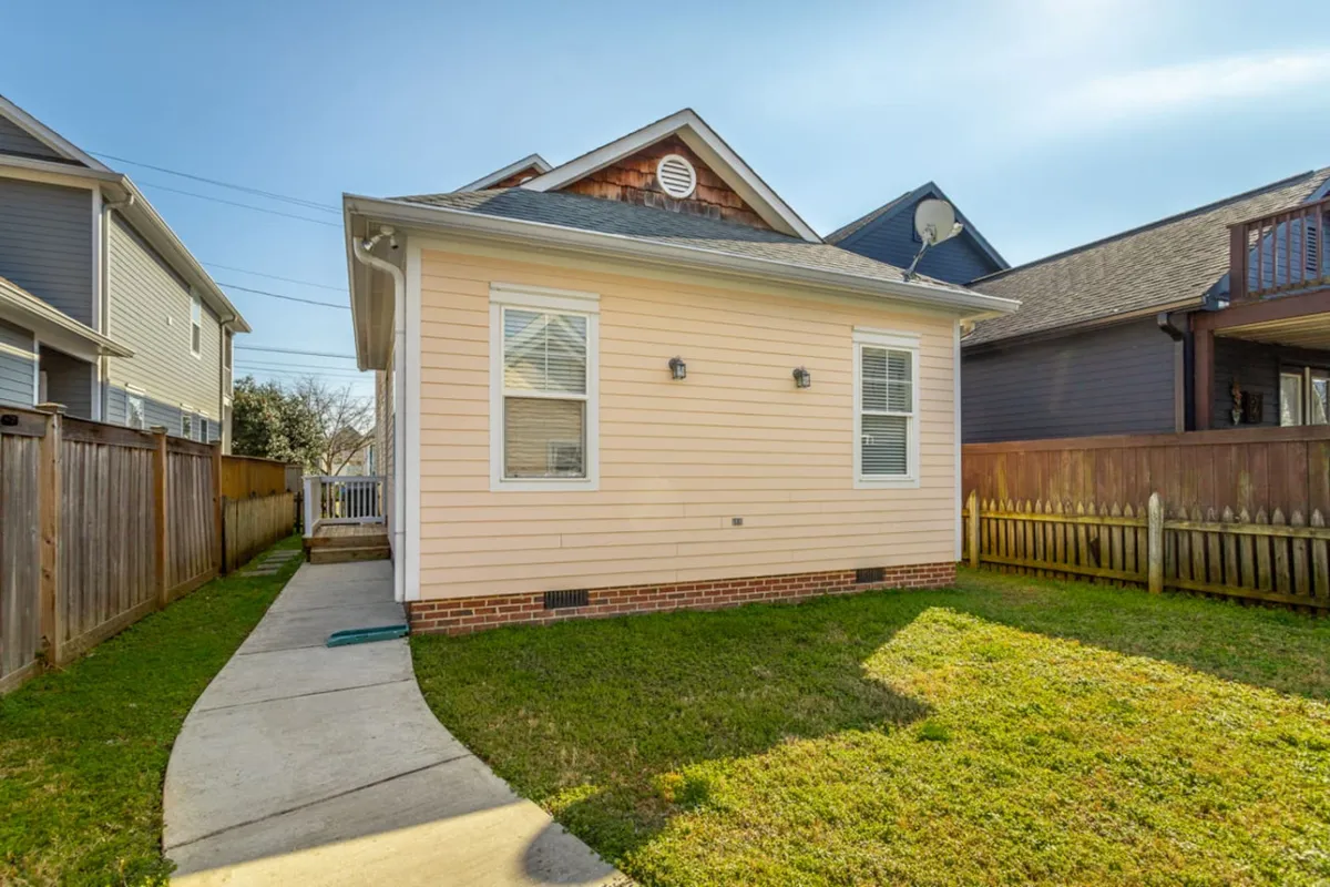 This image features the bright pink house facade with a well-kept lawn and a pathway leading to the entrance. The cheerful exterior suggests a welcoming, lively presence in the heart of the neighborhood.