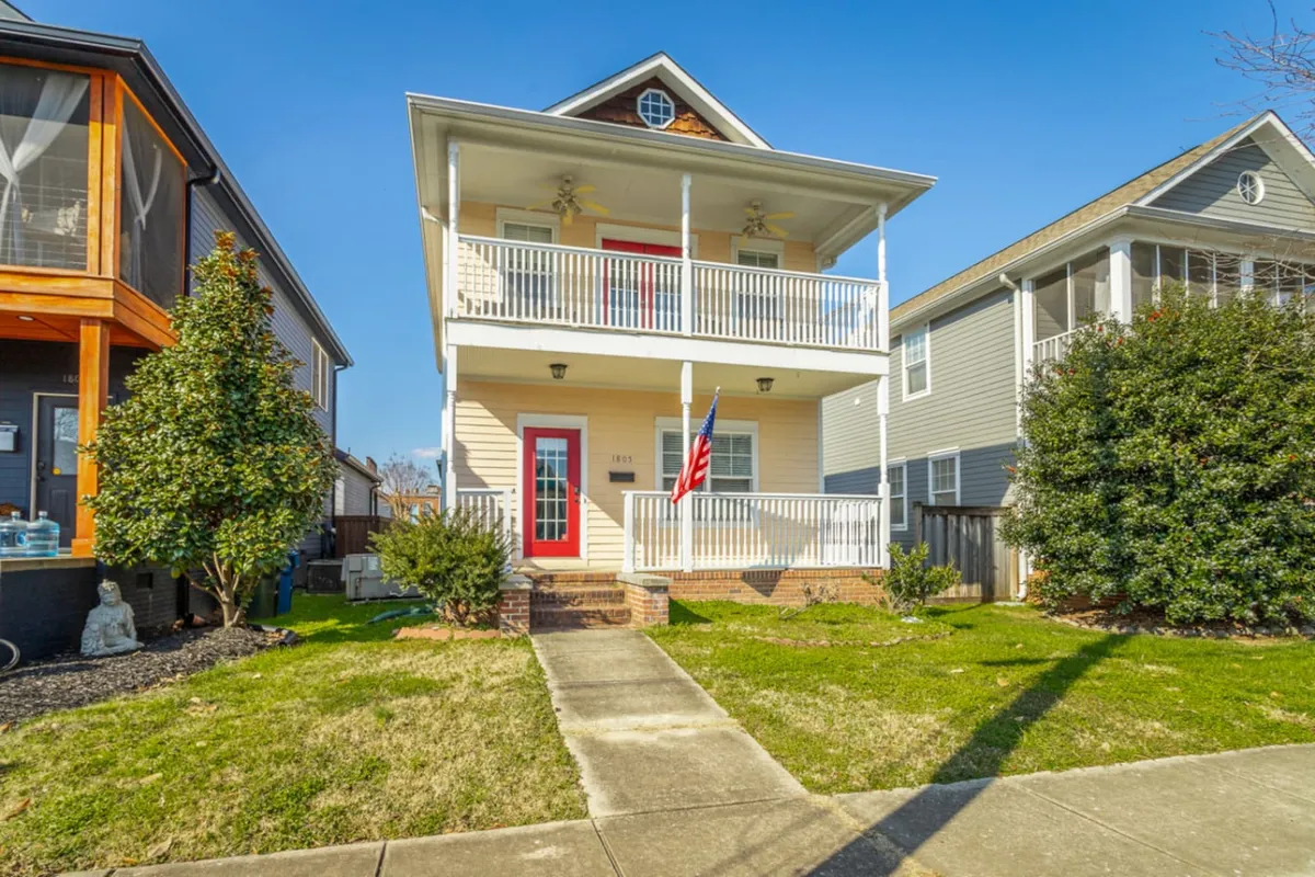 The image features the charming exterior of a downtown Chattanooga single-family home, showcasing a welcoming front porch adorned with a bold red door, an American flag fluttering above manicured landscaping, creating a friendly and inviting curb appeal.