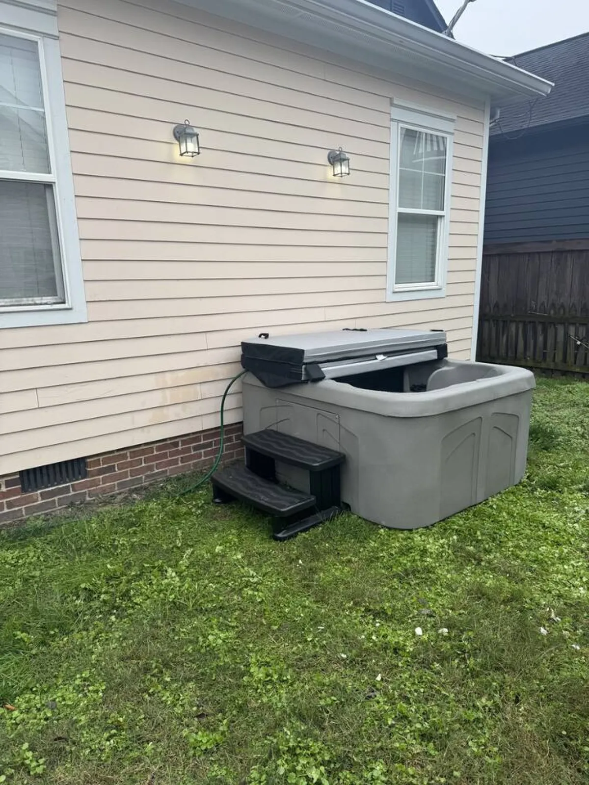This exterior image focuses on an inviting hot tub area adjacent to the building's exterior wall, illuminated by warm outdoor lighting. The scene suggests opportunities for relaxation and socializing in a private, secure setting that connects to the outdoors.