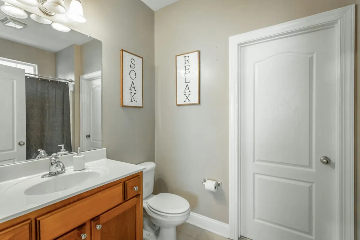A tranquil bathroom with a vanity sink, large mirror, and shower curtain. Framed signs reading 'SOAK' and 'RELAX' add to the calming ambiance, inviting guests to unwind and enjoy a restful bath or self-care routine.