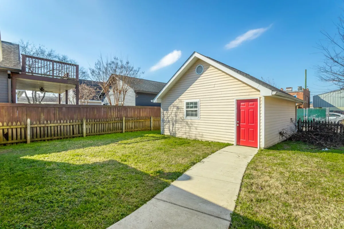 An exterior view of the home’s welcoming entry, featuring a vibrant red door, a well-kept lawn, and a fenced yard. The image conveys a sense of arrival, security, and warmth at first glance.